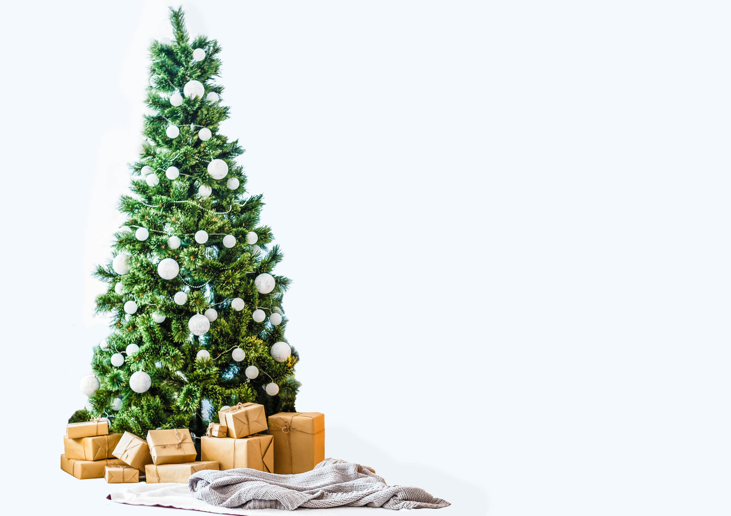 Big beautiful christmas tree decorated with beautiful shiny baubles and many different presents on wooden floor. White wall background with a lot of copy space for text. Close up