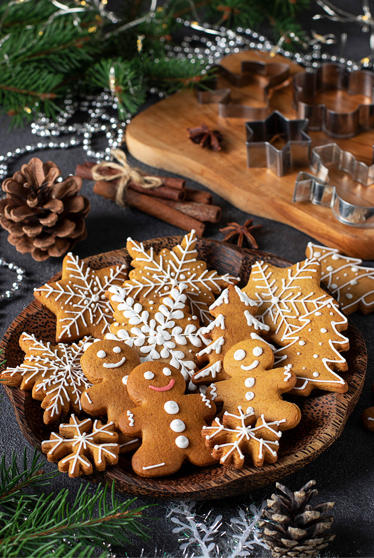 Gingerbread cookies in the form of fabulous gingerbread men, snowflakes and christmas trees on wooden plate in new year composition well as molds for gingerbread on a wooden board