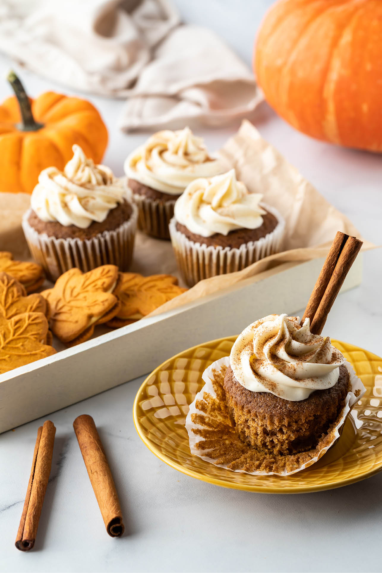 A tray of homemade pumpkin spice cupcakes and cookies with one cupcake in front on a plate.