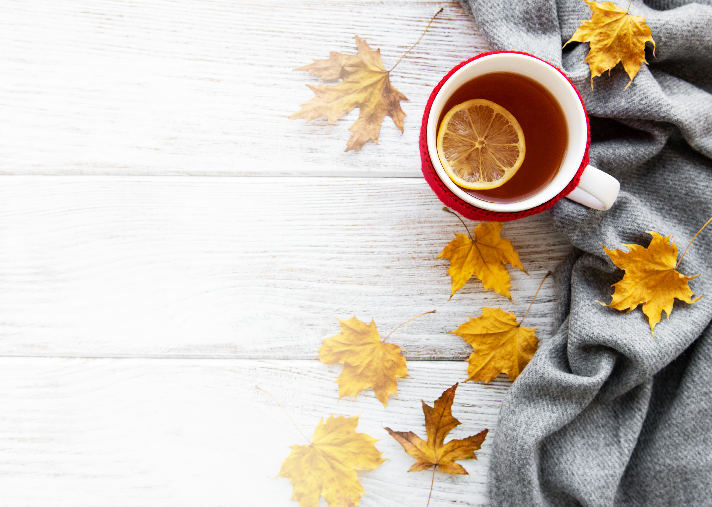 autumn flatlay on wooden backdrop with a cup of tea and fallen dry yellow leaves 